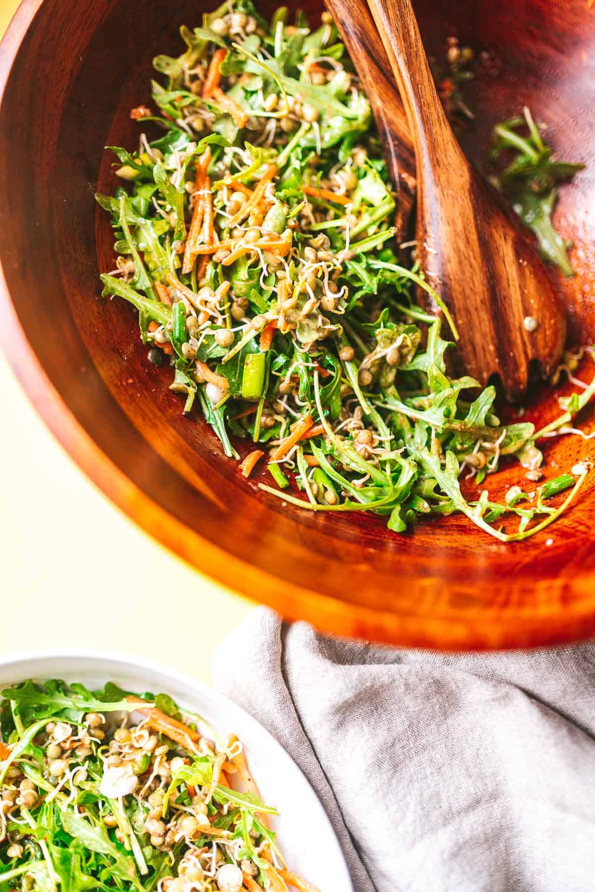 A wood salad bowl filled with green salad next to a white ceramic bowl filled with salad.