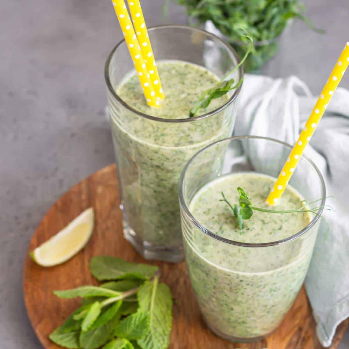 Two glasses of green smoothie on a wooden board.