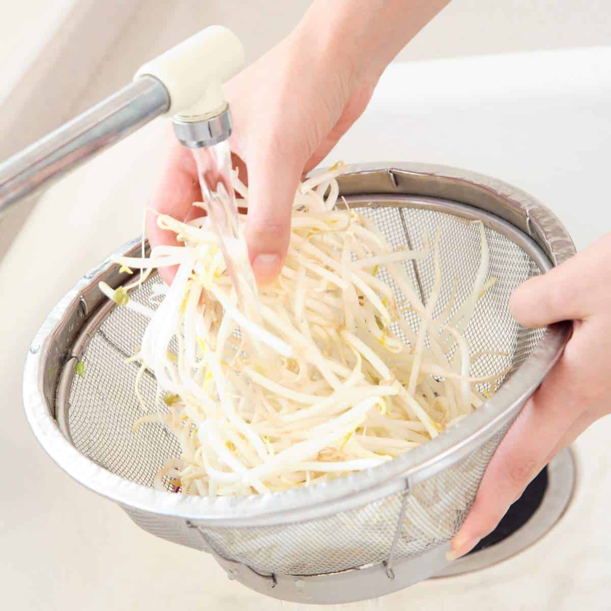 A person is squeezing a strainer full of steamed vegetables.