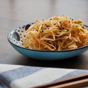 A bowl of noodles with sesame seeds and chopsticks.