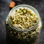 Sprouts in a glass jar on a table.