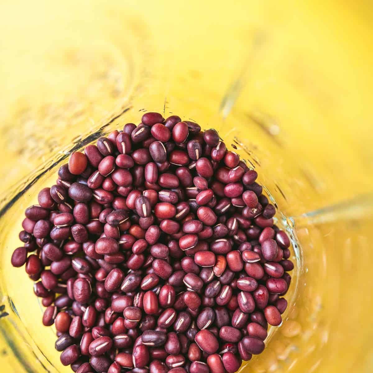 Red adzuki beans in a glass on a yellow background.