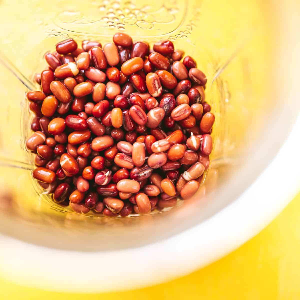 Red adzuki beans in a blender on a yellow background.