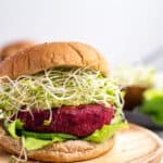 A beet burger with sprouts on a wooden cutting board.