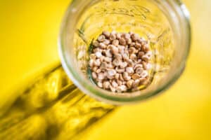 A glass jar containing dried chickpeas is placed on a bright yellow surface, casting a shadow to the left—perfect for learning how to sprout chickpeas at home.